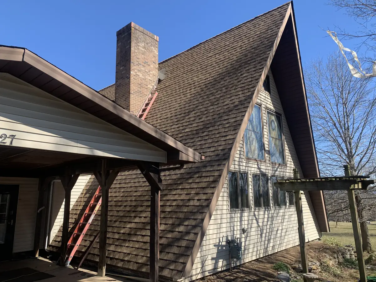A steep A-frame house with a brown shingle roof and a brick chimney