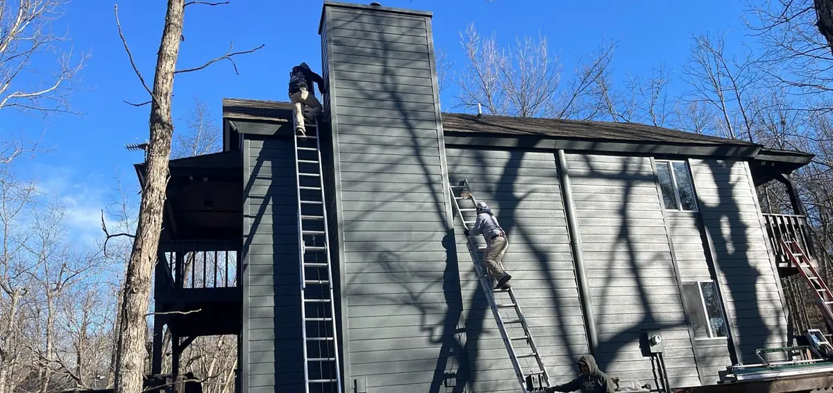 A tall blue house with a ladder and a crew member at work