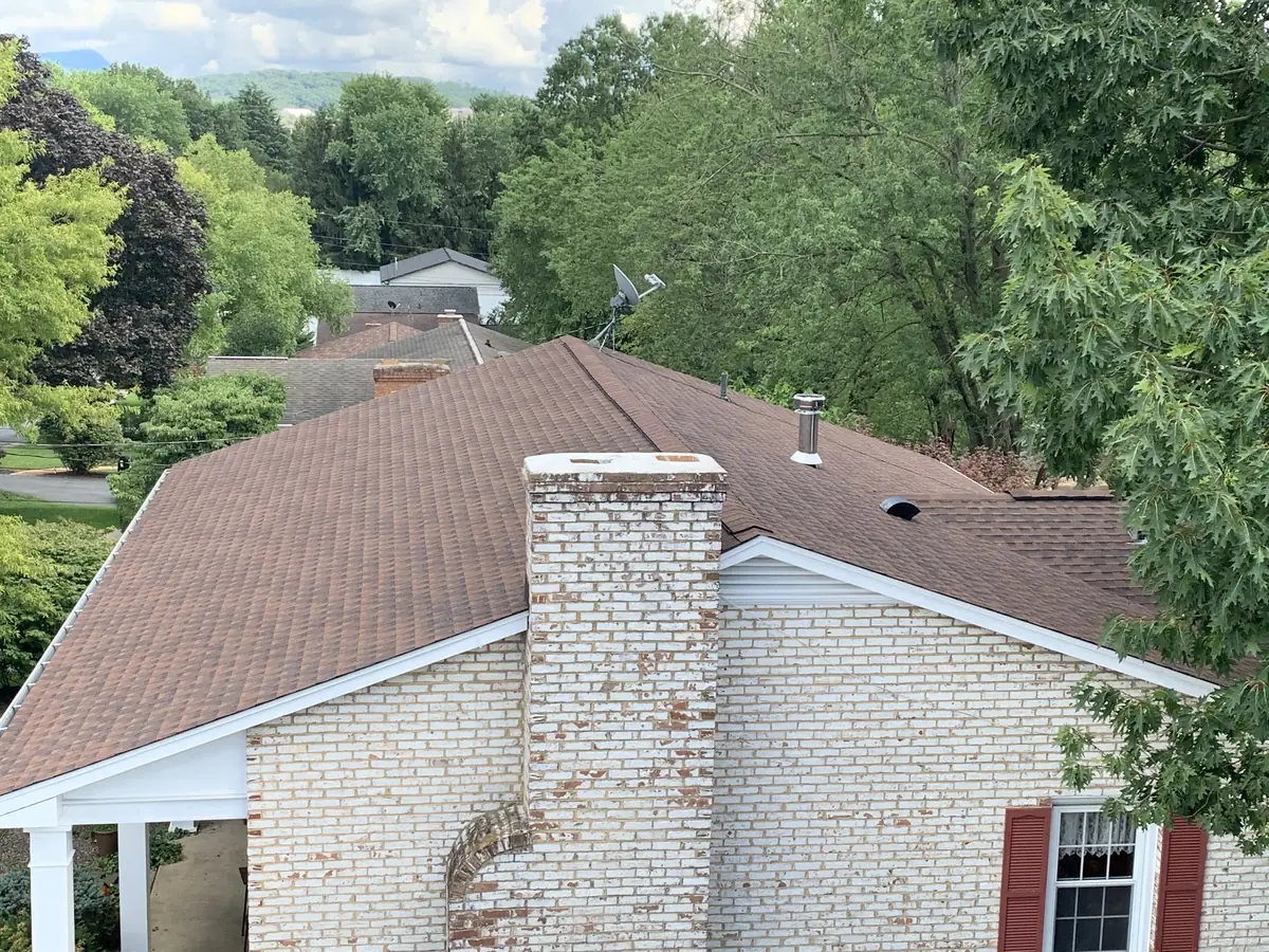 A brick house with a white chimney and a new brown shingle roof