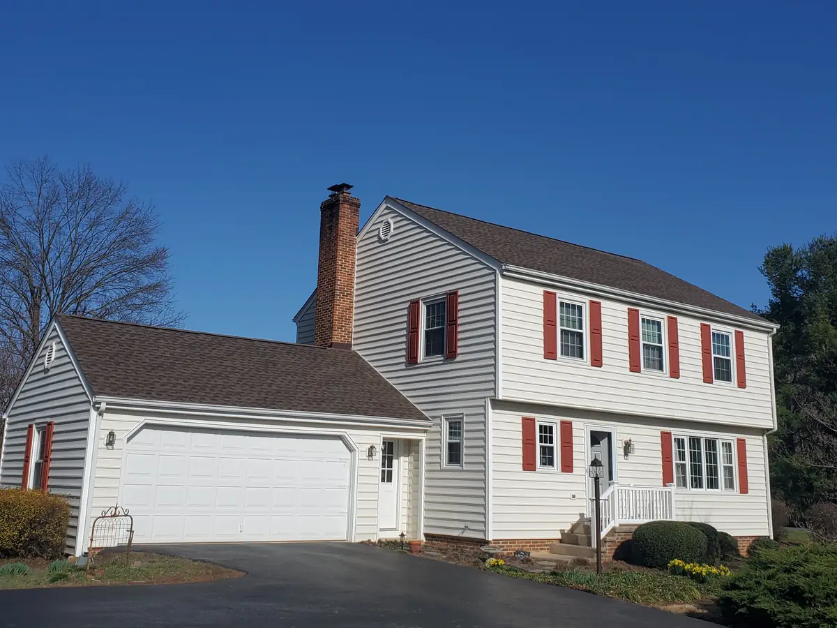 A white two-story colonial house with red shutters and a new brown shingle roof