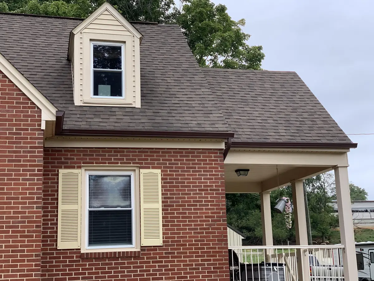 A brick house with a dormer and a front porch under a new roof