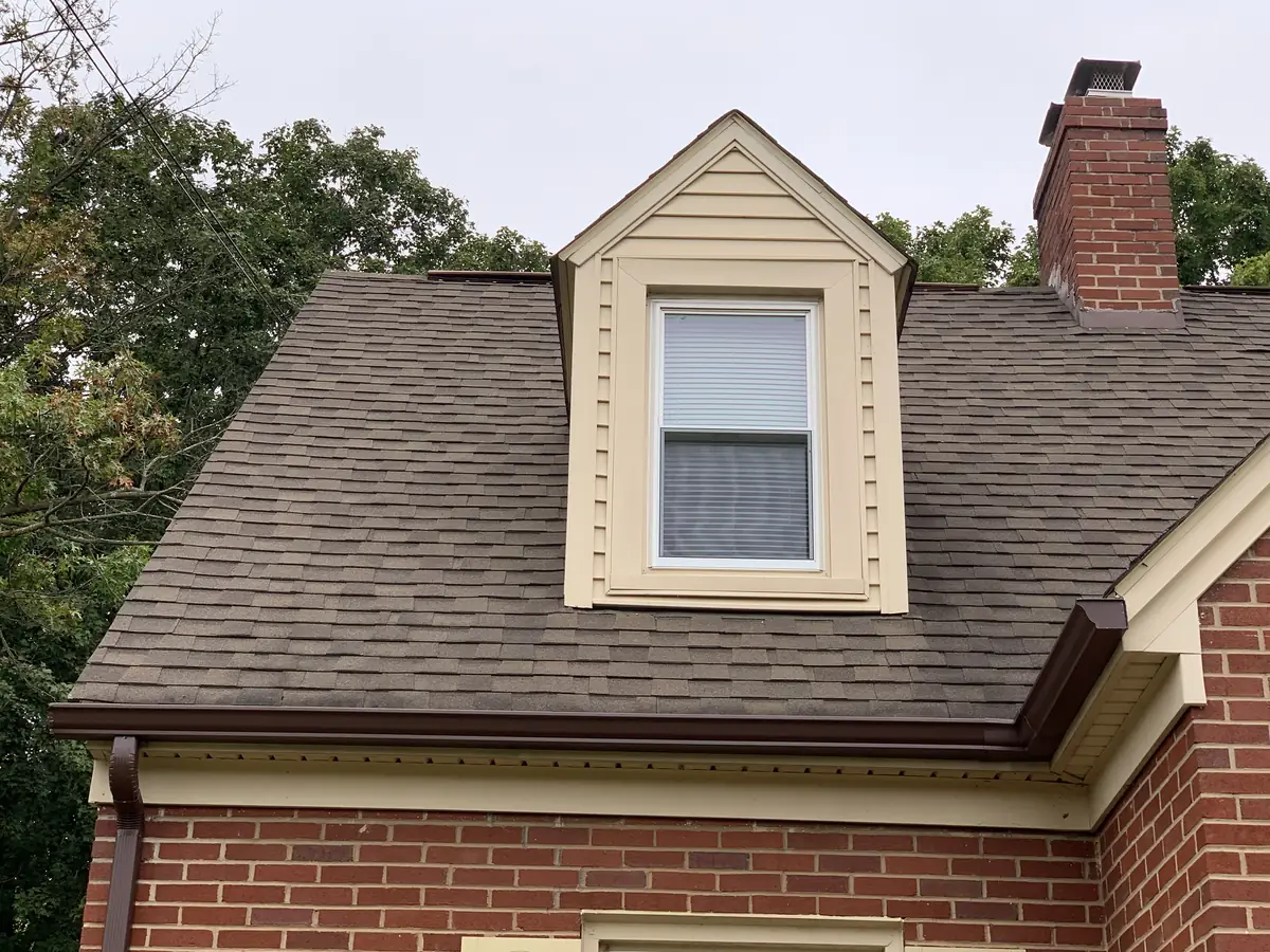 A dormer on a brick house under a brown shingle roof