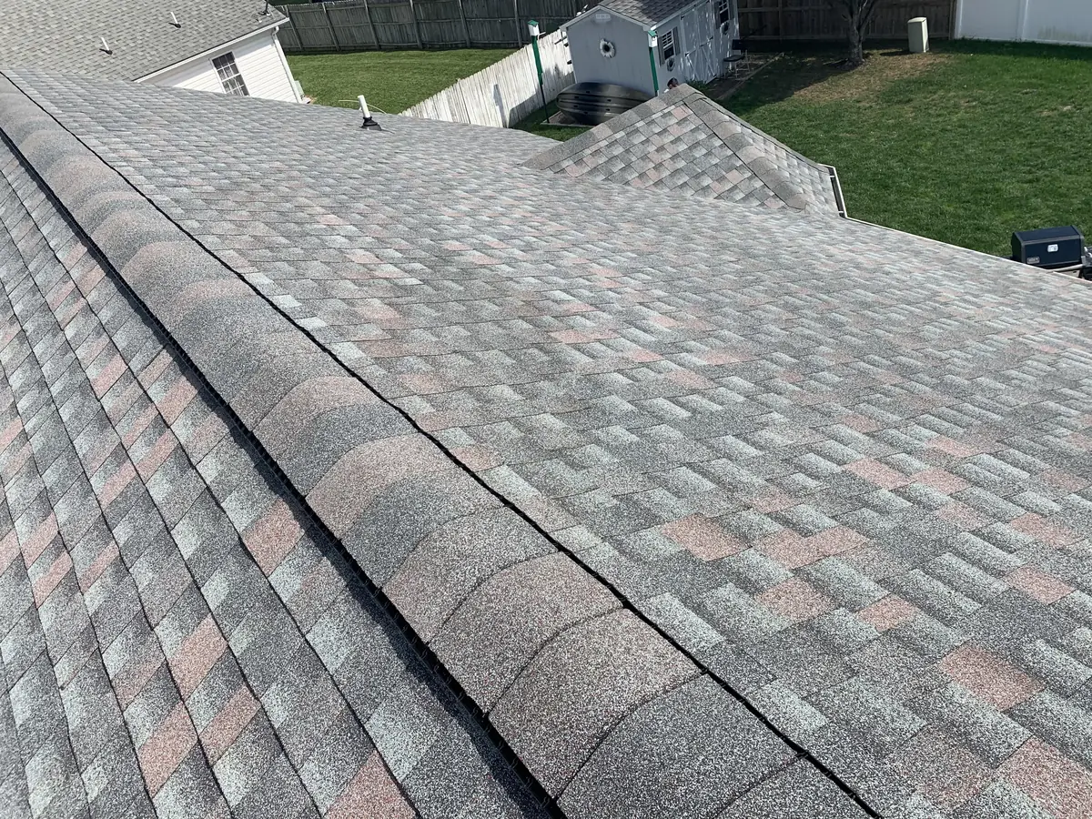 A gray shingle roof with a ridge cap above a lawn