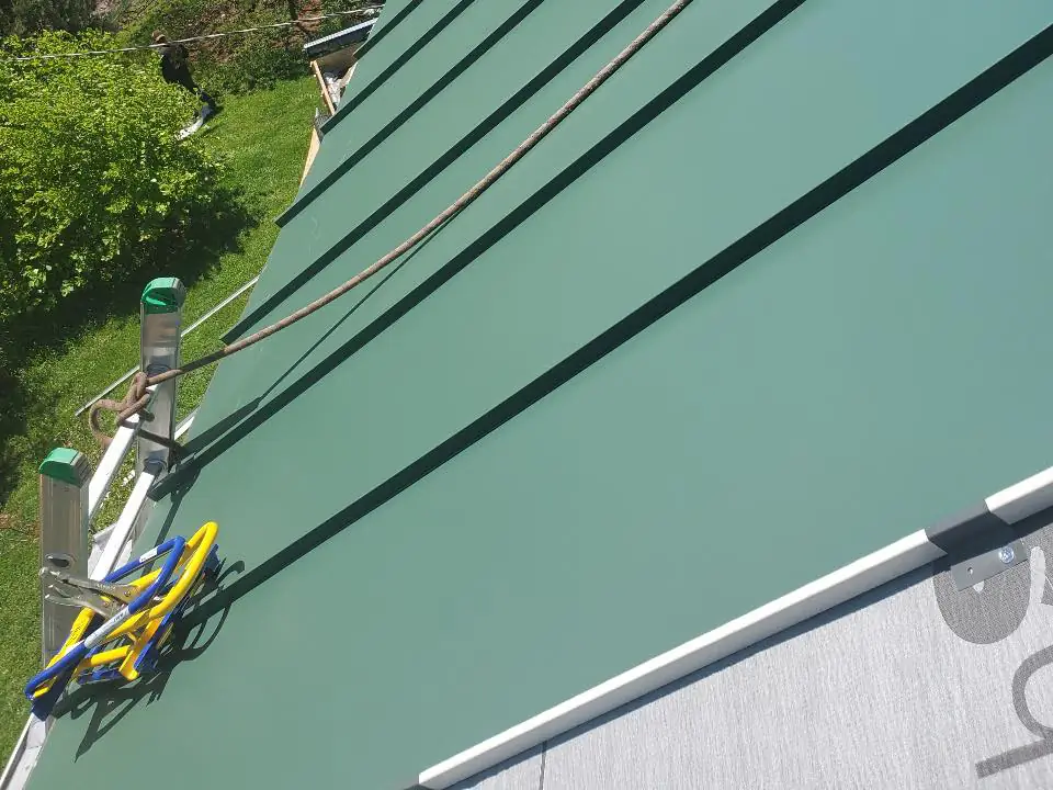 Green metal roof panels being installed, with a safety rope