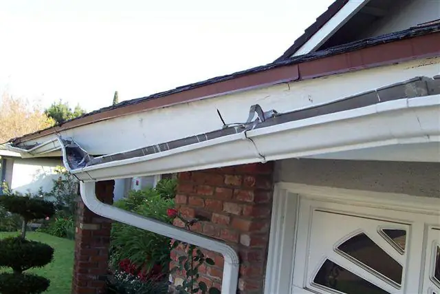 A white seamless gutter and downspout on a brick house