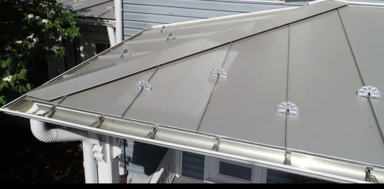A gray standing-seam metal roof with snow guards above a white gutter