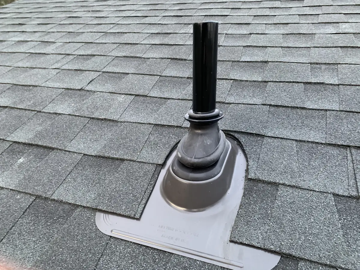 A new pipe boot sealing a vent pipe through gray shingles