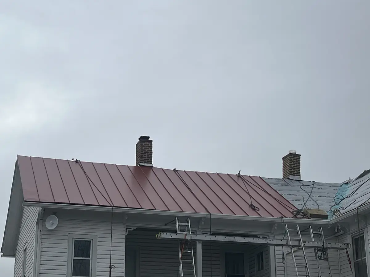 A red standing-seam roof on a white house, with ladders