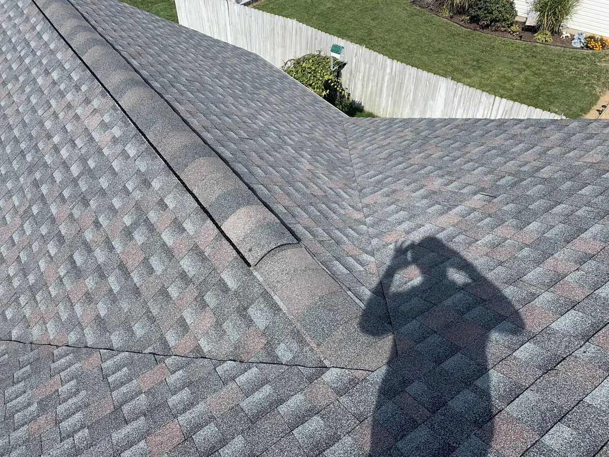 A roofer's shadow on a new gray shingle roof, beside the ridge cap