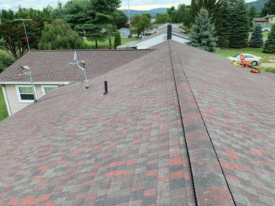 A red and gray shingle roof ridge with trees and hills beyond