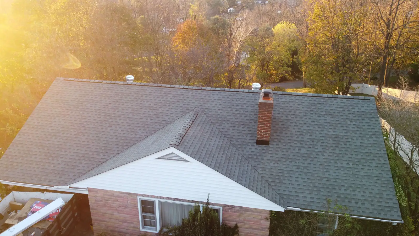 A gray shingle roof with a brick chimney in low autumn sun