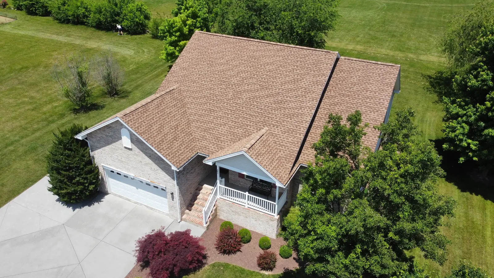 A brick house with a tan shingle roof and porch, seen from the air